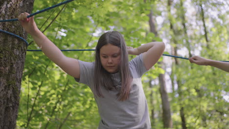 active child fearlessly climbs the ropes between the trees. girl in an adventure park are pass obstacles on the rope road. children camp summer camp