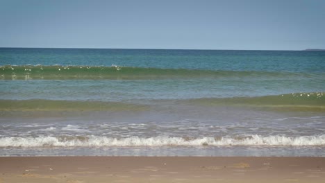 Beautiful-blue-waves-crushing-on-a-sandy-beach-on-a-sunny-day-in-the-Magdalen-Islands-in-slow-motion