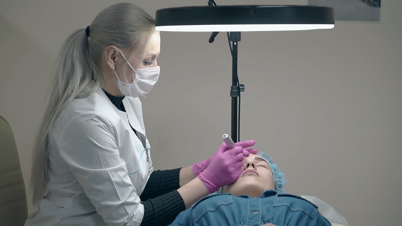 cosmetician applies eyebrow makeup under black round lamp
