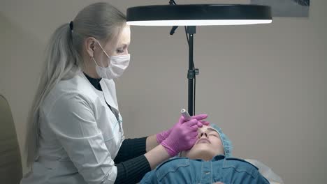 cosmetician-applies-eyebrow-makeup-under-black-round-lamp