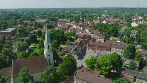 Aerial-establishing-view-of-Kuldiga-Old-Town-,-houses-with-red-roof-tiles,-Evangelical-Lutheran-Church-of-Saint-Catherine,-summer-day,-travel-destination,-drone-shot-moving-forward