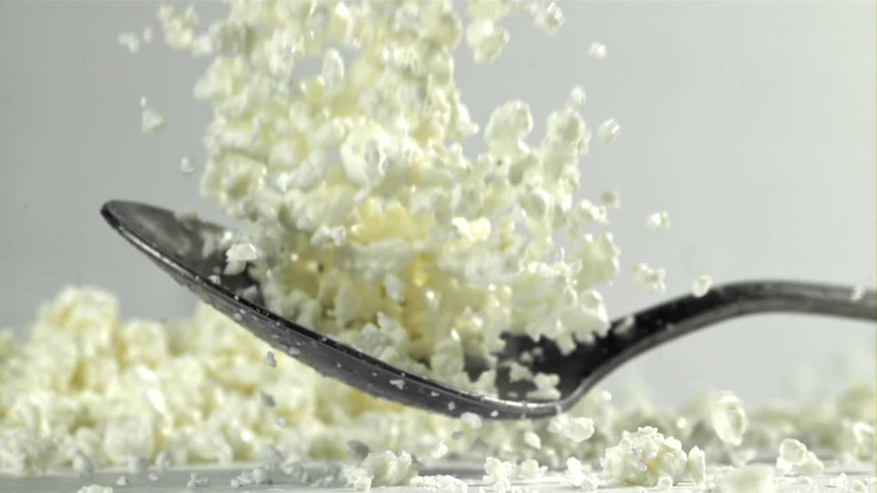 Frisk hytteost falder fra en ske i slowmotion