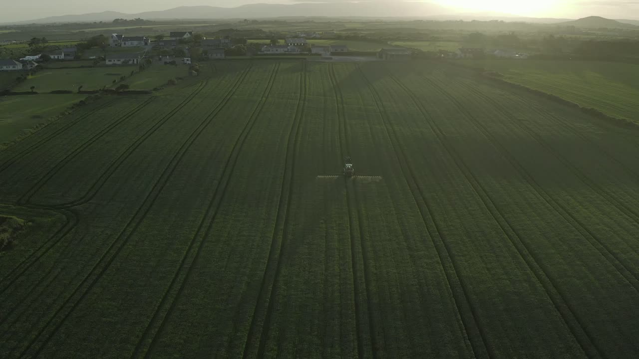 Beautiful misty sunset aerial of tractor on green field spraying crop