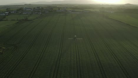 beautiful misty sunset aerial of tractor on green field spraying crop