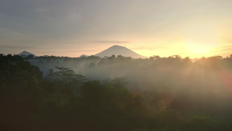 Video-Cinematográfico-De-Un-Dron-Volando-A-Través-De-Una-Palmera-Para-Revelar-La-Selva-Tropical-Y-El-Majestuoso-Volcán-Monte-Agung-Al-Amanecer-Ubicado-En-Bali,-Indonesia