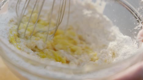 person whisking eggs and batter mixture in bowl