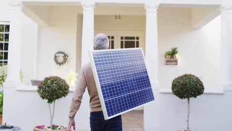 hombre caucásico feliz usando guantes, sosteniendo el panel solar y caminando