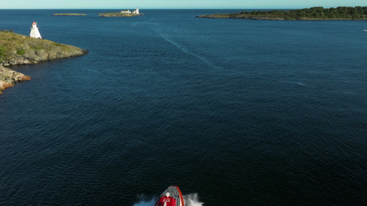 A tugboat cruises through a narrow waterway, leaving a wake behind. Rocky shores line both sides, while distant lighthouses stand tall under a clear blue sky