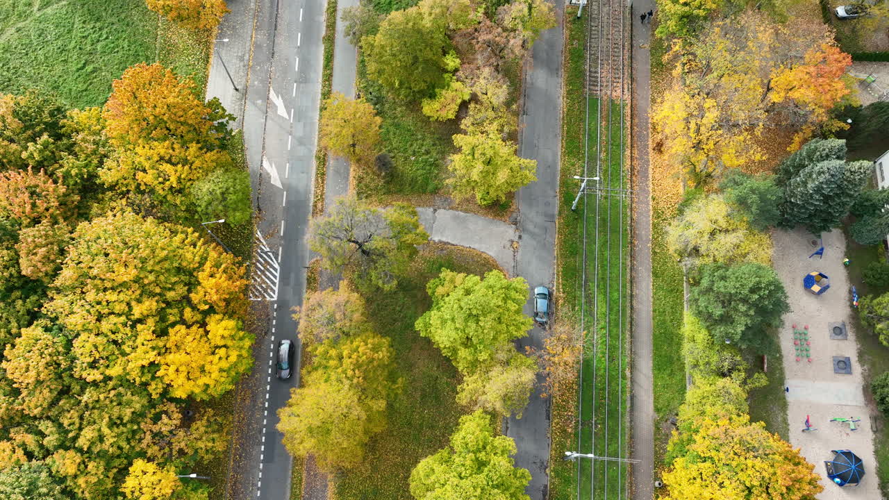 Aerial shot of road and tram tracks surrounded by colorful autumn trees