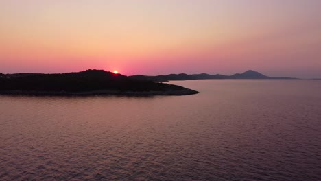 flying-up,-revealing-colourful-sunset-above-an-island-with-vegetation-and-hills