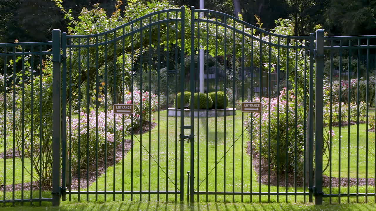 Cancello metallico chiuso che custodisce l'ingresso di un giardino pubblico in una giornata soleggiata e luminosa.