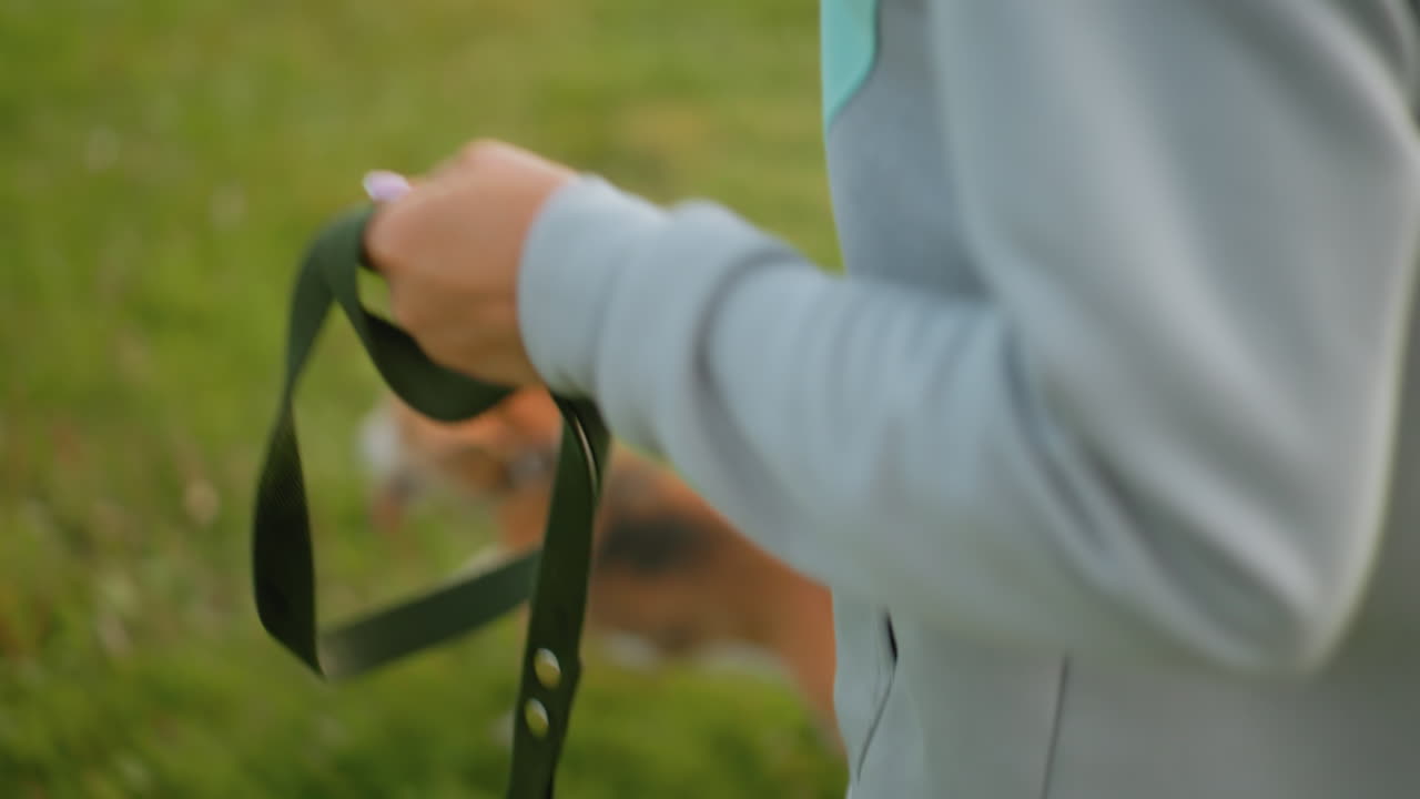 Trainer jogging with leather leash in hands across grassy park wearing sportswear relaxed movement holding pet gear during outdoor workout sunny weather focus on leash and athletic wear