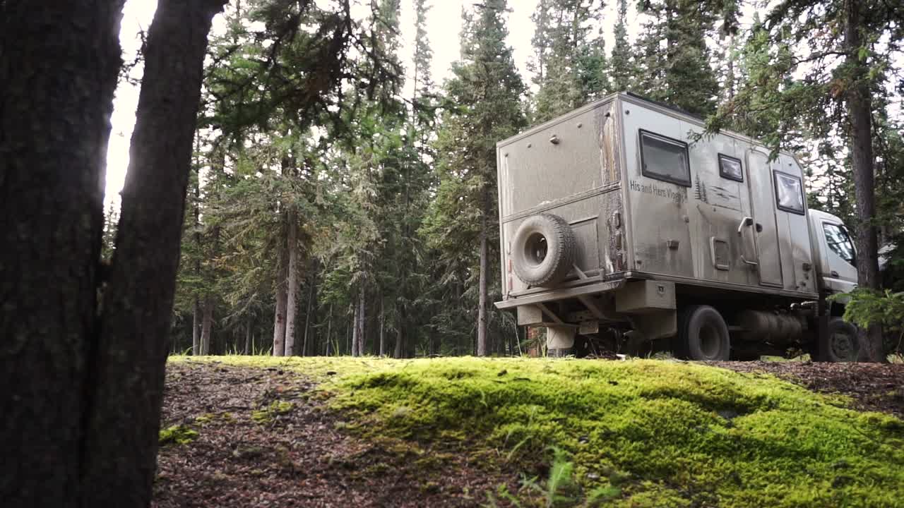 알래스카 유콘 지역의 아름다운 녹색 숲에 있는 비포장 도로에서 멀리 떨어져 있는 대형 오프로드 캠퍼 밴의 정적인 샷