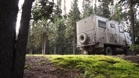 static shot of a large off road camper van an pulling away on a dirt road in a beautiful green forest in the yukon region of alaska