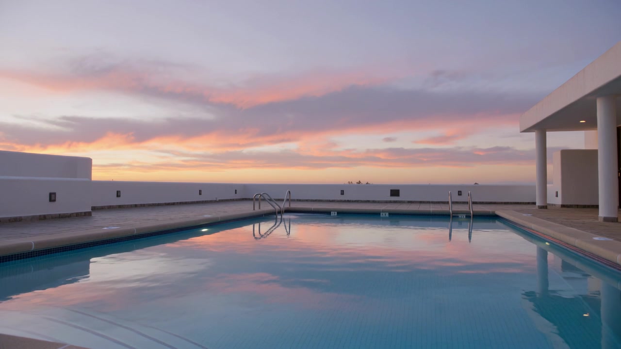 Reflecting rooftop pool showing pastel sunset while light fading and breeze making ripples, ladders