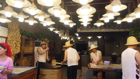 xian, china -  july 2019 :  two men hitting hard with big wooden hammers to crack grain which will be used in making of sweet snack for sale on the street, muslim quarter
