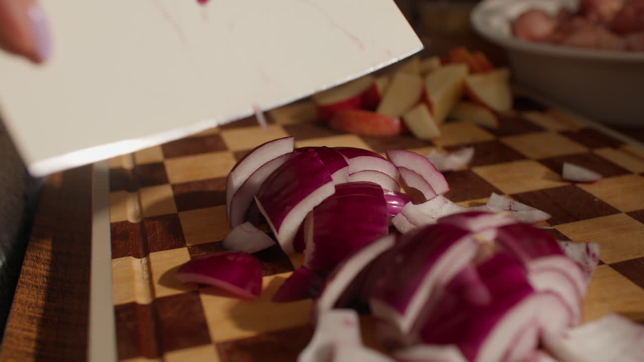 Person chops red onion on wooden board in warm kitchen setting
