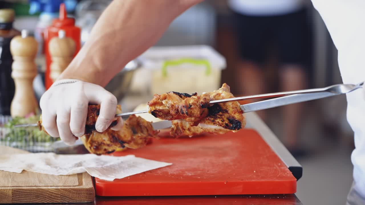 Chef puts ready barbeque. Cook takes roasted juicy meat from skewers and puts on a dish. Tasty shashlik ready to eat in the restaurant.