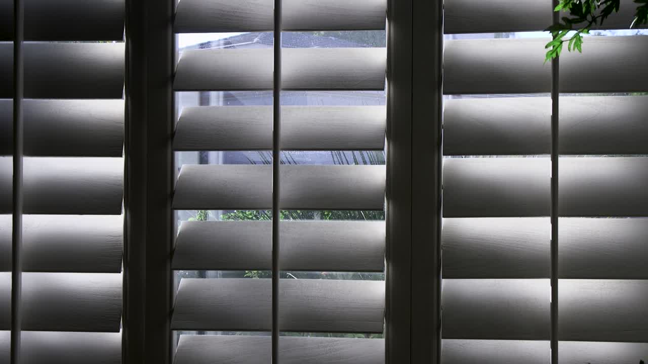 Shadows move back and forth across the louvers of white wooden shutters