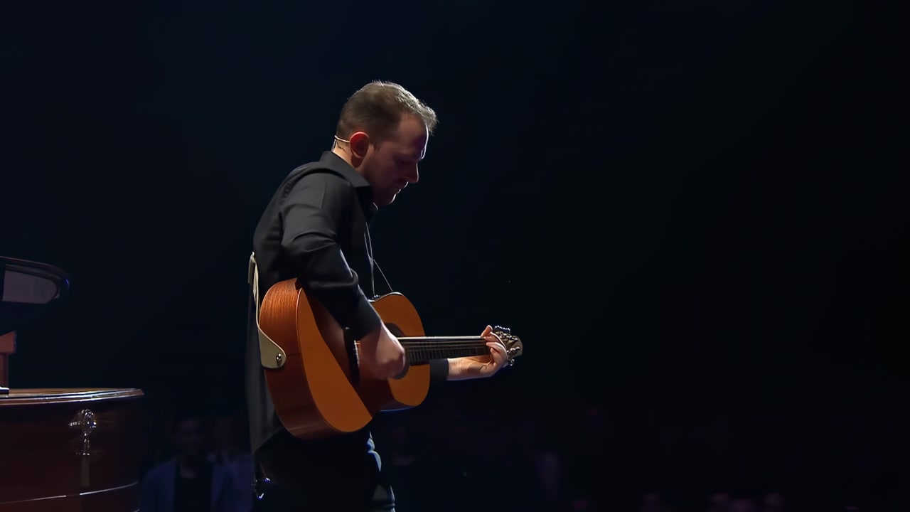 Mandlig guitarist på mørk scene spiller akustisk guitar under en enkelt spotlight med klaver ved siden, klimprer.
