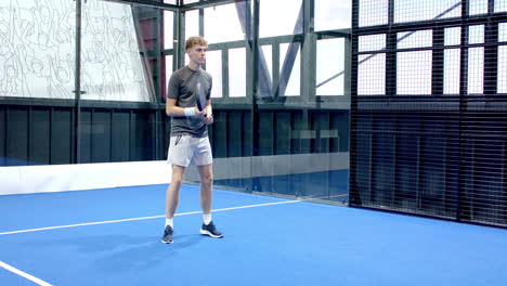 Young man playing padel tennis on blue on indoor court, focused and ready to hit, copy space