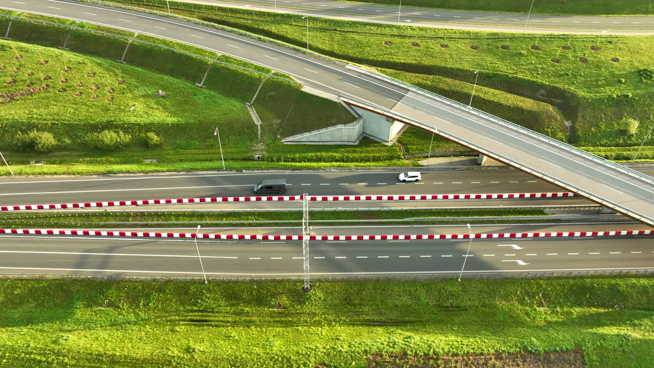 High-angle drone view of an expressway overpass near Gdynia, showing light traffic beneath the bridge and flanked by lush green grassy embankments