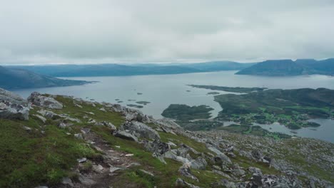 Hombre-Caminando-Por-La-Colina-Rocosa-De-La-Montaña-Con-Vistas-Al-Fiordo-En-Noruega