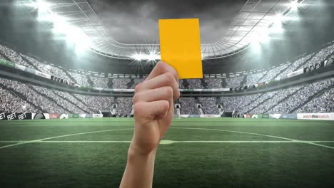 Animation-of-hand-holding-yellow-card-over-stadium