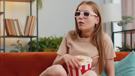 Woman-sitting-on-couch-eating-popcorn-and-watching-interesting-TV-3D-film,-sport-game-online-at-home