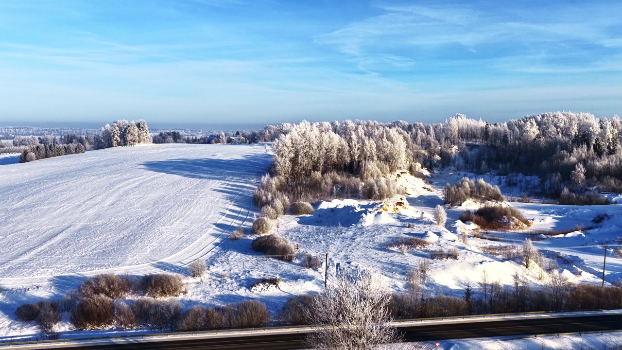 Winter landscape with snowy rural road and hoarfrost covered trees on a sunny day
