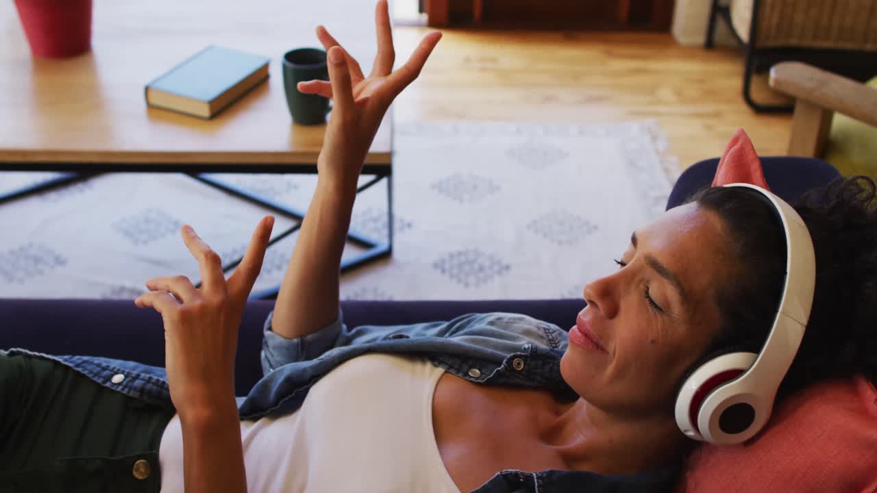 Caucasian woman listening to music with headphones on, lying on sofa at home