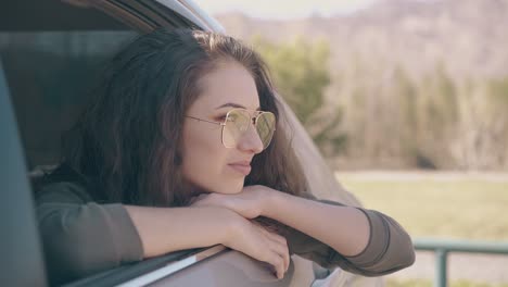 serious girl with long brown hair sits by open car window