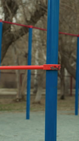 close-up of blue and red iron bars in a stadium, with two benches positioned in the middle, with barren trees and passing cars visible in the background