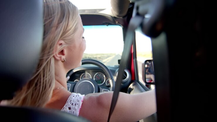Giovane donna caucasica guida un'auto in una giornata di sole durante un viaggio su strada, con spazio per il testo.