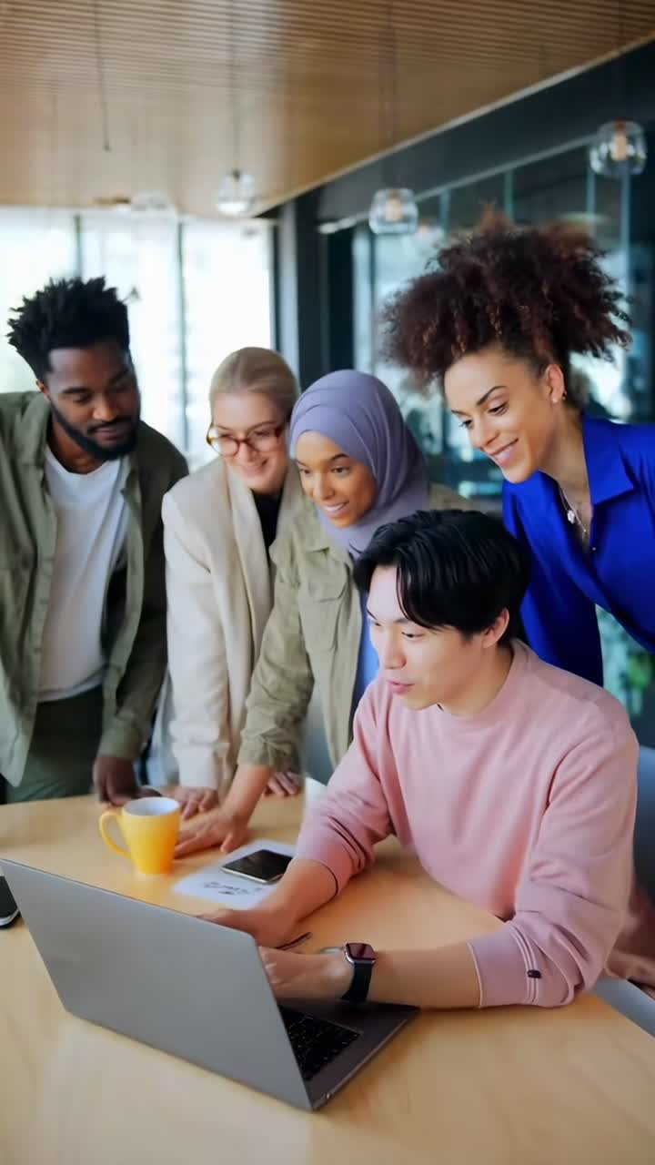 High-angle video of a diverse team collaborating around a laptop in a modern office