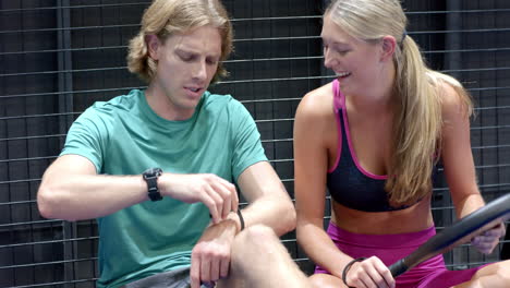 man and woman enjoying padel tennis break, smiling and examining equipment together, at indoor court