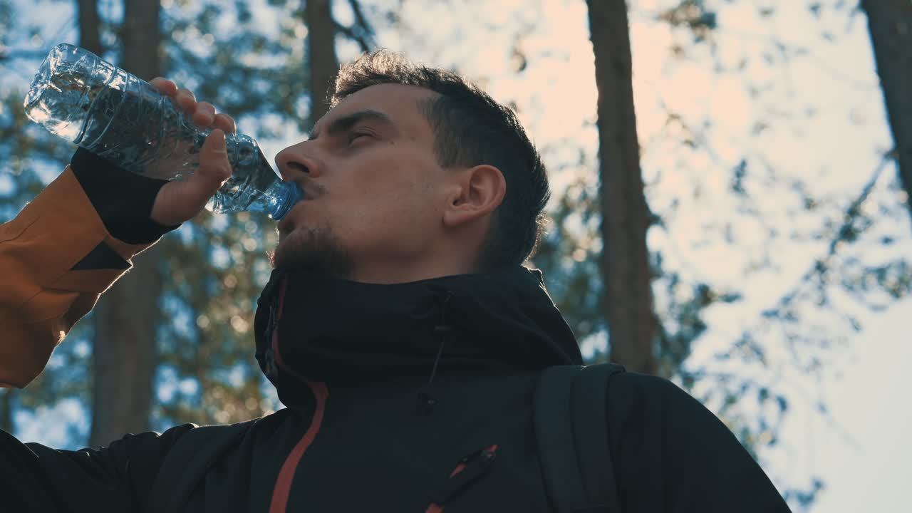 el excursionista en el bosque bebe agua de la botella de plástico 4k
