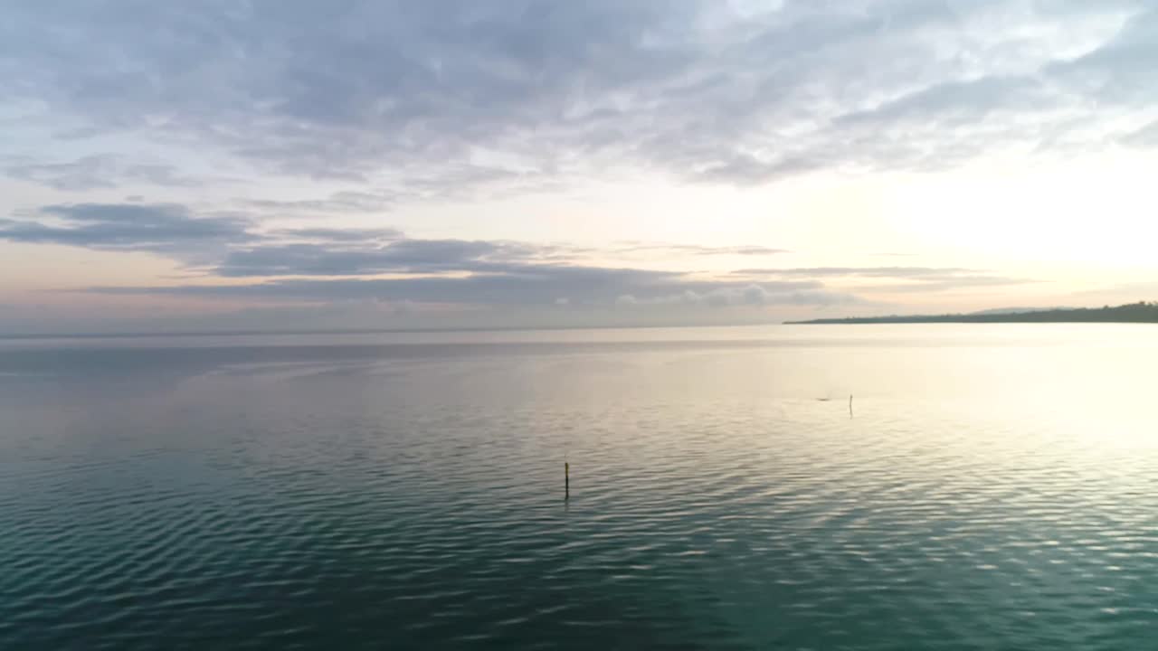 Drone Panning Over blue tranquil Water and soft clouds in the horizon at sunrise