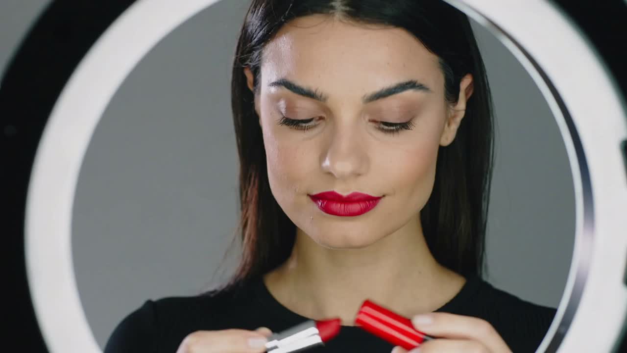 Applying woman placing silver lipstick on upper lower lip checking finish in ring light black top