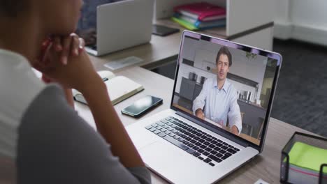 sección media de una mujer afroamericana haciendo una videollamada con un colega masculino en una computadora portátil en la oficina