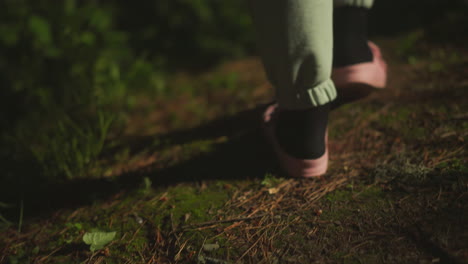 female person in warm socks and comfortable pink slippers walks along illuminated path near house. lady returning home after long day of activity in nature