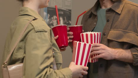 glückliches paar mit popcornbox und alkoholfreien getränken, die miteinander sprechen und ein wandplakat im kino betrachten