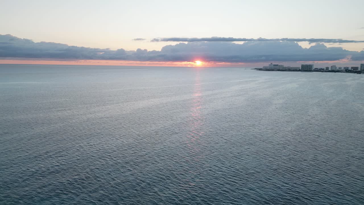 Sunset over Cancun's Playa Langosta with ocean waves and distant city skyline