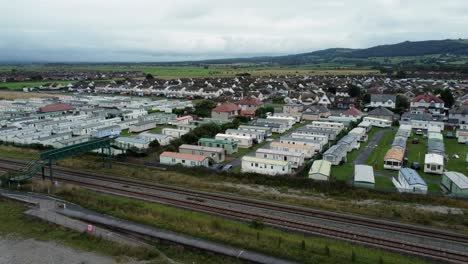 Static-caravan-trailer-beachfront-staycation-holiday-home-campground-resort-aerial-view-low-angle-left-pan-above-railway-tracks