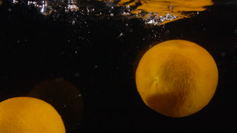 muchos limones amarillos frescos en cámara lenta salpican en el agua con burbujas