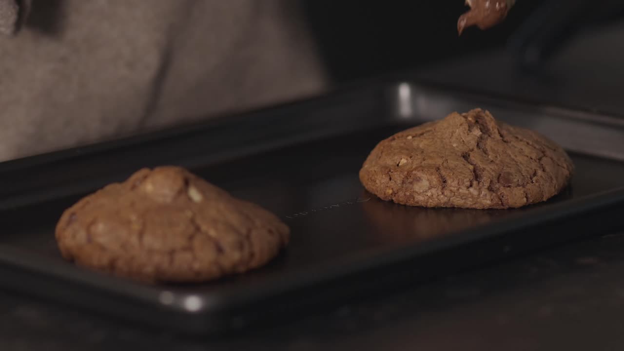Close up of spoon adding chocolate topping onto cookie dough on tray