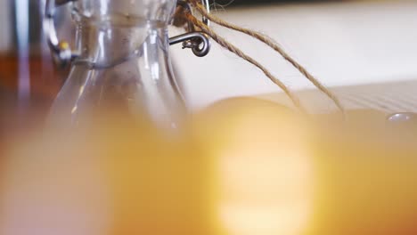 blurry candle lit in front of glass bottle with tag and band, slider close up