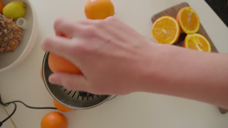 naranjas frescas siendo exprimidas a mano en un exprimidor eléctrico en casa