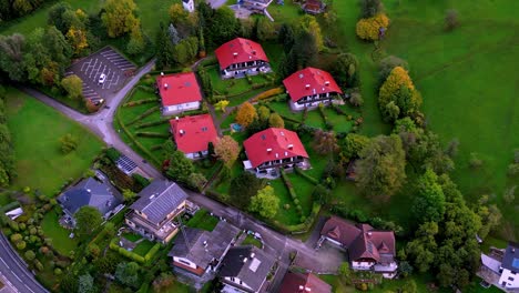 una vista aérea de un tranquilo barrio residencial con coloridos techos rojos ubicados en medio de exuberantes colinas verdes y un río sinuoso bajo un cielo azul claro