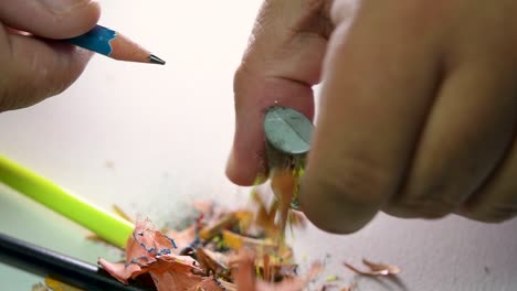 imágenes de manos afilando lentamente un lápiz y algunos lápices de colores con un sacapuntas de cuña